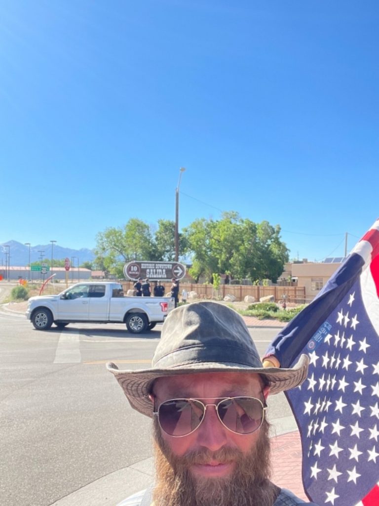 Danny Taylor taking a selfie while holding an upside down american flag. There are police on the other side of the street behind him.